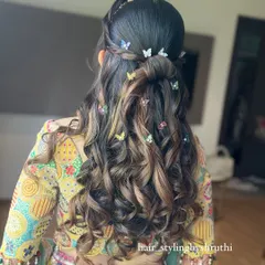 A playful and modern half-up hairstyle with voluminous curls, perfect for a Mehendi or Sangeet ceremony. The style is accented with whimsical multi-colored butterfly clips, adding a touch of personality and charm.