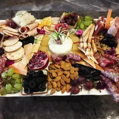 This is our grand charcuterie platter, a feast of textures and flavors. It features a curated selection of imported cheeses, cured meats, fresh fruits like pomegranates and grapes, assorted nuts, olives, and artisanal crackers.