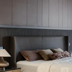 This sophisticated bedroom features a winged headboard in dark leather, set against a modern, paneled wall. The design creates a cozy, enclosed feeling, perfect for a restful night's sleep.