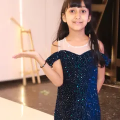 A young girl in a sparkling blue dress strikes a graceful pose for her portrait.
