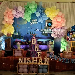An underwater-themed first birthday party, complete with a custom backdrop, a colorful balloon arch, and marquee letters spelling out "ONE". A photo display on an easel adds a personal touch.