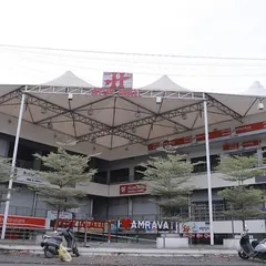 A street-level view of the completed Ayur Mall, showing the prominent tensile roof structure that covers the central atrium. This architectural element provides shelter while allowing natural light, creating a bright and welcoming food court and plaza area.