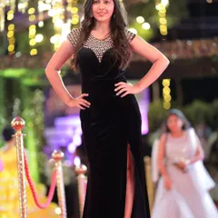 A full-length shot of an actress on the red carpet, capturing her confident pose and elegant black gown against the backdrop of event lighting.