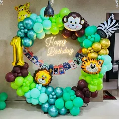 A circular balloon frame for a jungle-themed first birthday. This unique design incorporates animal head foil balloons, a photo banner of the baby's first year, and a central neon 'Happy Birthday' sign.