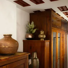 A detail shot showcasing the home's timeless tribute to heritage. Antique brass and copper vessels are displayed against rich, dark wood cabinetry and a traditional waffle slab ceiling.
