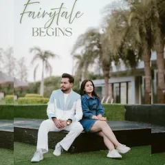 A bright and happy portrait of a couple in stylish casual wear, set against the backdrop of a modern home with lush greenery. The text "Fairytale Begins" adds a touch of romance.