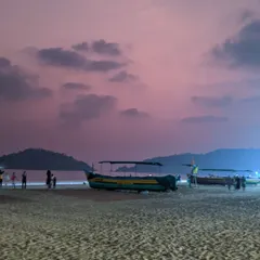 An evening at Palolem beach in South Goa. The sky is painted in soft hues of pink and purple after sunset, creating a calm and beautiful scene with fishing boats resting on the sand.