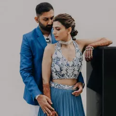 A stylish couple portrait from a pre-wedding carnival party. The groom embraces his bride, whose modern blue lehenga and intricate henna stand out beautifully.