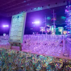 The bar area, where the iridescent theme continued. The bar front was wrapped in shimmering material, complemented by a custom menu and an elegant display of glassware, all under a soft purple glow.