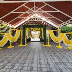 A traditional wedding entrance arch decorated with lush green foliage and garlands of yellow and white flowers, creating a warm and auspicious welcome for guests.