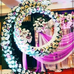 An elaborate floral crescent moon structure, perfect for a unique naming ceremony or cradle ceremony backdrop. The dense arrangement of white and purple flowers creates a dreamy and magical setting.