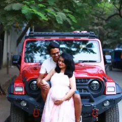A cool, modern maternity shot with the couple posing on the front of a red jeep, blending urban style with the joy of expectancy.