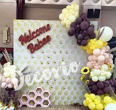 This "Welcome Babee" backdrop features a honeycomb pattern and is framed by a unique balloon garland. The use of pampas grass and sunflowers adds a rustic, boho touch to the bee-themed baby shower.