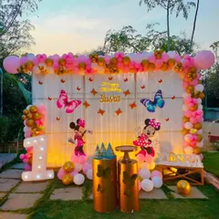 A classic theme that never fails to delight. This Minnie Mouse first birthday party features a full-stage backdrop with pink and gold balloons, butterfly accents, character cutouts, and a light-up marquee number '1'.