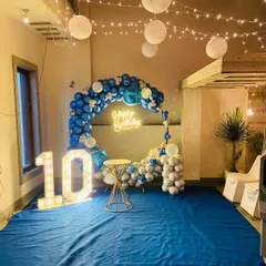 This circular balloon arch in shades of blue and silver creates a dynamic backdrop for any celebration. Complete with a "Happy Birthday" neon sign and marquee numbers, this setup is perfect for making a statement in any indoor or terrace space.