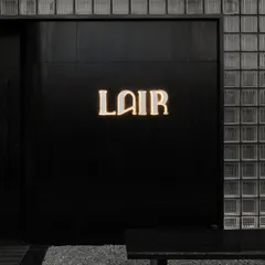 The entrance to Lair in Gurgaon, where a wall of glass bricks conceals the speakeasy within. The minimalist black facade and glowing logo create a sense of mystery and exclusivity, setting the stage for the dramatic interior narrative.