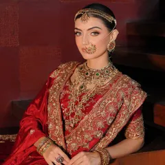 A close-up on the essence of a traditional bride. The styling focuses on the layering of jewellery, from the nath to the choker and rani haar, complementing the rich red Akriti by Shakun lehenga.