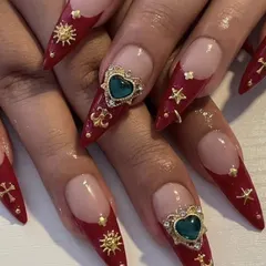 This dramatic red stiletto set is adorned with gold charms and large, heart-shaped green gems, creating a regal and opulent look.