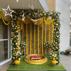 For traditional functions, I create elegant backdrops like this one. It features a full frame decorated with yellow marigold and white flower garlands, with hanging star lights and a central 'urli' for a classic and auspicious look.