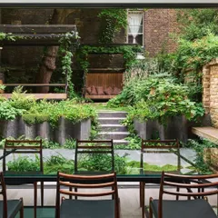 A view from a dining room looking out onto a multi-level urban garden. We used raised planters, a wooden pergola, and dense foliage to create a lush, green oasis in a compact city backyard.