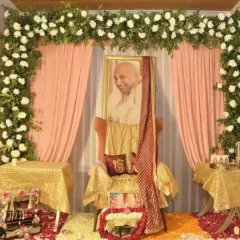Here is another style for a Guru Ji event, featuring a floral arch of white carnations over soft peach drapes. The altar uses golden fabrics and a deep red sash to create a warm and respectful setting, with rose petals scattered on the floor.
