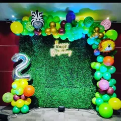 For a kid's second birthday, I made this jungle theme decoration. The setup features a green grass wall, a balloon arch with animal foils, a 'Happy Birthday' neon sign, and a number '2' balloon pillar.