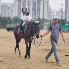 Safety is paramount, especially with our youngest riders. A trainer carefully leads the horse while a mother and child enjoy a ride together in our arena.