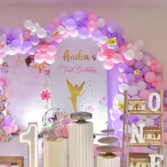 For this fairy-themed first birthday, I used a soft palette of pink, purple, and white balloons to create a dreamy arch. The decor is personalized with light-up numbers and the baby's name.