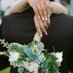 A bride's hands, adorned with beautiful nails and rings, holding her bouquet from behind her groom. This detailed shot from Anu and Nikhil's wedding is a beautiful symbol of their union.