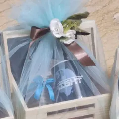 A corporate gift hamper packed in a wooden crate and wrapped in light blue tulle with a brown ribbon and white rose.