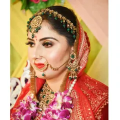A close-up of a bride's makeup and jewellery. The look features a classic red lip, a beautiful green and gold jewellery set, and a traditional nath.