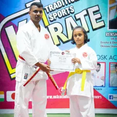 A young student proudly receives her official certificate after successfully passing her belt grading examination. This formal recognition is an important part of building self-esteem in children.