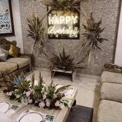 I designed this modern birthday party decor for a client's home. The setup features a trendy 'Happy Birthday' neon sign on a backdrop decorated with dried pampas grass, creating a stylish and rustic vibe. The matching centerpiece on the coffee table ties the whole room together.