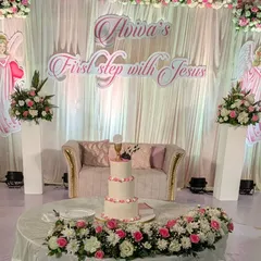 The cake table and stage backdrop for Aviva's 'First step with Jesus.' The design features angelic cutouts, soft draping, and beautiful floral arrangements in a pastel pink and white palette.