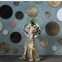 A full-length shot against a wall of circular marble samples, playing with pattern and texture. The model's pose and avant-garde styling create a visually interesting and artistic fashion statement.