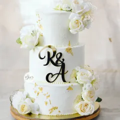A different angle of this beautiful white wedding cake, showing the custom initial topper and the careful placement of each floral arrangement.