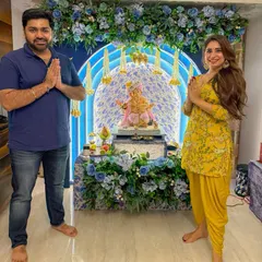 A happy client posing with the 'Aqua Blue' Ganpati decor. This setup features a beautiful floral arch and traditional hanging elements, creating a picture perfect corner for festive family photos.