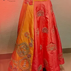 This handcrafted lehenga choli is a celebration of tradition. The rich orange and red raw silk skirt features delicate lotus embroidery, while the blouse is adorned with sparkling stone detailing, making it a timeless piece for any bride.