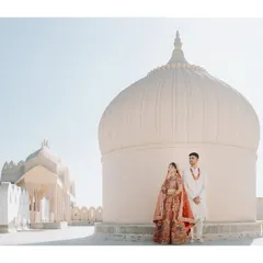 The couple stands against the sun-drenched domes of a Rajasthani palace. This wide shot captures the scale and serene beauty of a destination wedding in the heart of India.