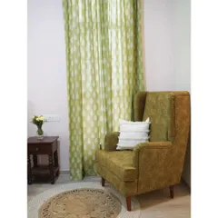 A cozy corner in the guest bedroom, featuring a comfortable wingback chair in a rich green upholstery. The leaf-patterned curtains and jute rug complete the nature-inspired, tranquil vibe of the room.