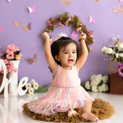A moment of pure celebration captured before the cake smash, with the birthday girl in a rainbow dress against a lavender butterfly backdrop.