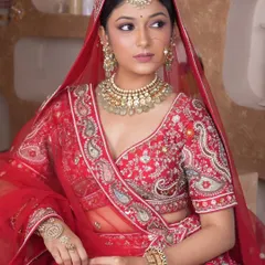 A classic red bridal look featuring a Kundan choker with light green bead drops, a matching maang tikka, and a traditional nath. This set is perfect for the quintessential Indian bride.