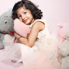 A sweet toddler hugs her stuffed animals. This gentle studio portrait with a soft pink background highlights the innocence and comfort of childhood.