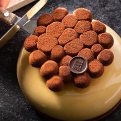 Capturing the moment of anticipation. A knife gently touches the top of this stunning entremet, adding a dynamic element and highlighting the dessert's delicate structure.