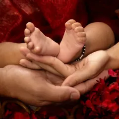 A close-up shot that tells a big story. A parent's hands gently cradle their baby's tiny feet, symbolizing protection, love, and the start of a new journey together.