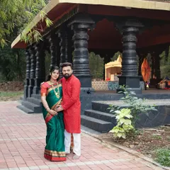 A beautiful full length portrait of the couple at a location with traditional architecture. This shot showcases their coordinated ethnic outfits and the serene setting of their cultural maternity shoot.