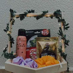 This hexagon-shaped wooden basket is filled with a mix of fun and practical items. It includes a deodorant, a face mask, colorful scrunchies, and a variety of chocolates.