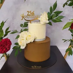 A closer look at the 25th-anniversary cake, highlighting the smooth finish and the elegant arrangement of white roses. The custom gold acrylic topper adds a personalized touch to celebrate this major milestone.