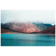 A moody, atmospheric shot of Pangong Lake, with low clouds shrouding the colorful, mineral-rich mountains.