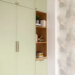 This sage green wardrobe includes a built-in open bookshelf, adding both storage and a decorative element. It’s a practical solution for keeping books and favorite objects on display in a bedroom.